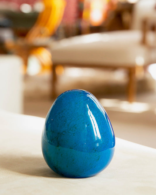 Blue decorative egg on a surface with a blurred indoor setting