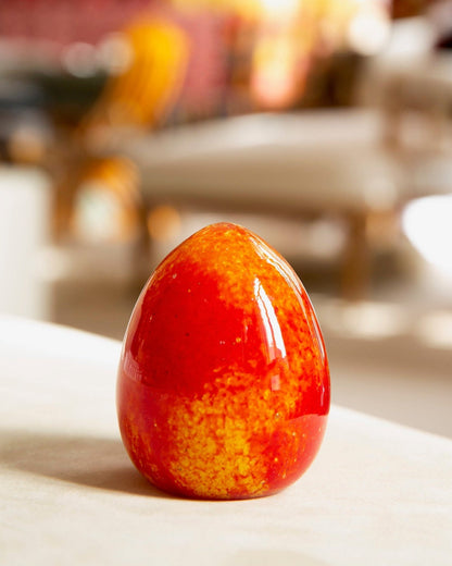 Red and orange speckled egg on a white surface with blurred background