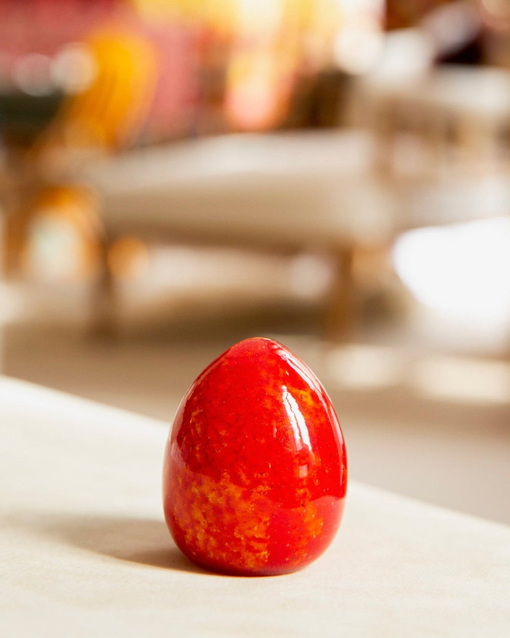 Red decorative egg on a surface with blurred chairs in the background