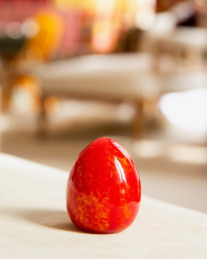 Red decorative egg on a surface with blurred chairs in the background